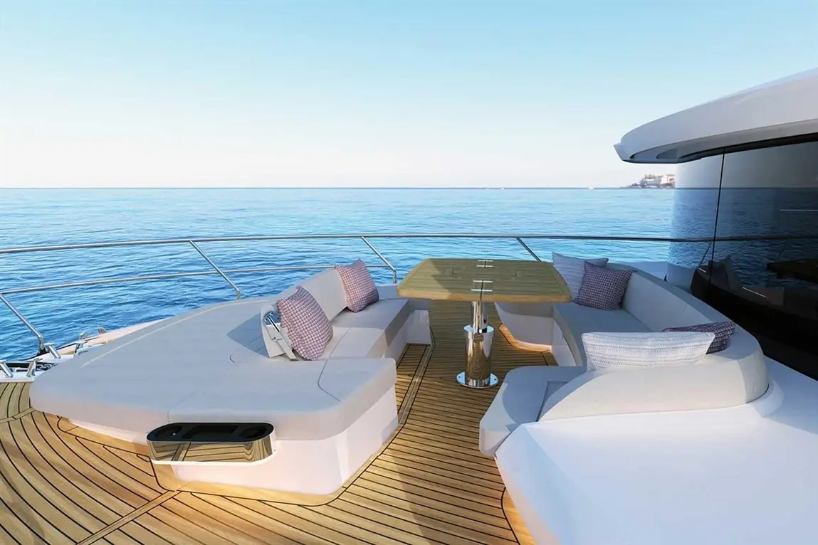 Luxury yacht deck featuring a seating area with cushions and a wooden table, overlooking a serene sea under a clear sky.