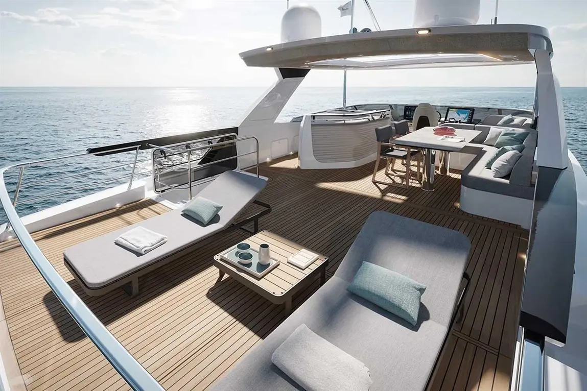 Luxury yacht deck with sun loungers, a dining table, and stunning ocean views under bright sunlight.