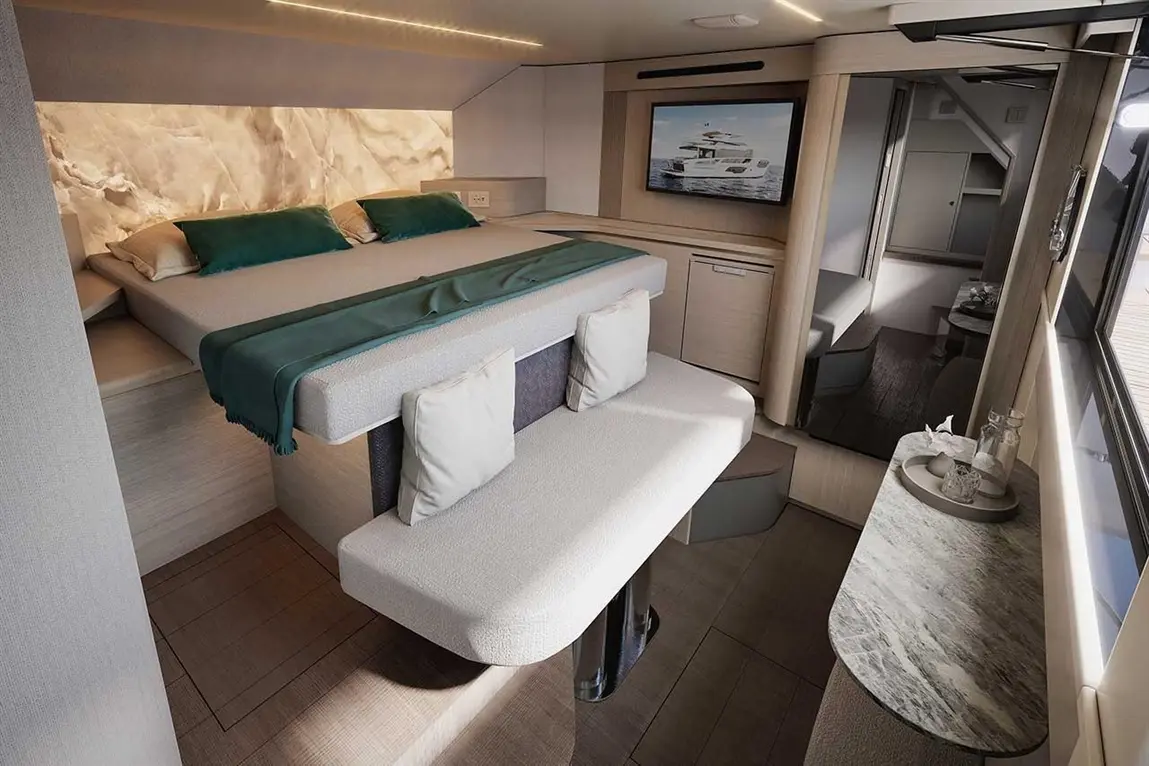 Modern yacht interior featuring a double bed, seating area with pillows, wooden flooring, and a TV displaying a yacht image.