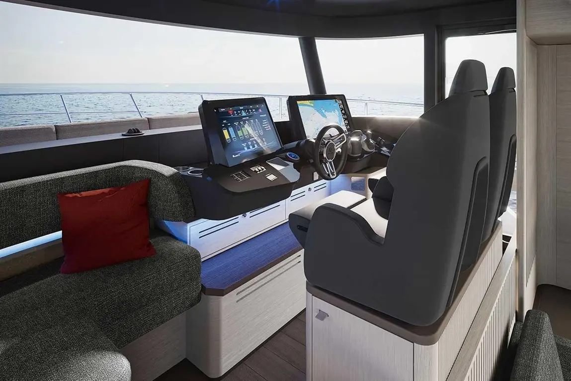 Modern yacht interior with dual screens displaying navigation, steering wheel, and plush seating area with a red cushion.