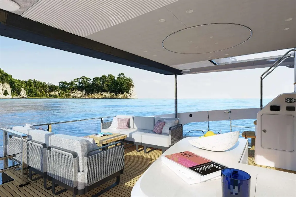 Luxurious yacht interior with seating, table, books, and a view of calm blue waters and a lush green shoreline.