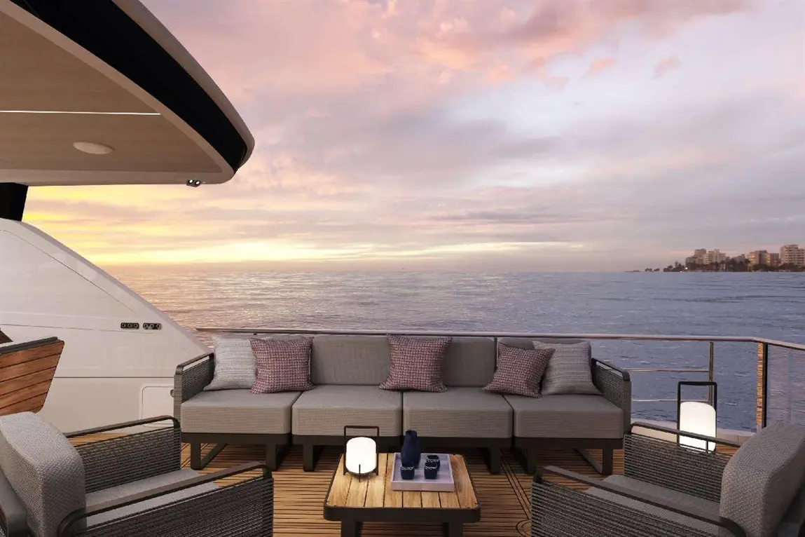 Stylish yacht deck seating with grey cushions, a wooden table, and a scenic ocean sunset backdrop. Relaxation space at sea.