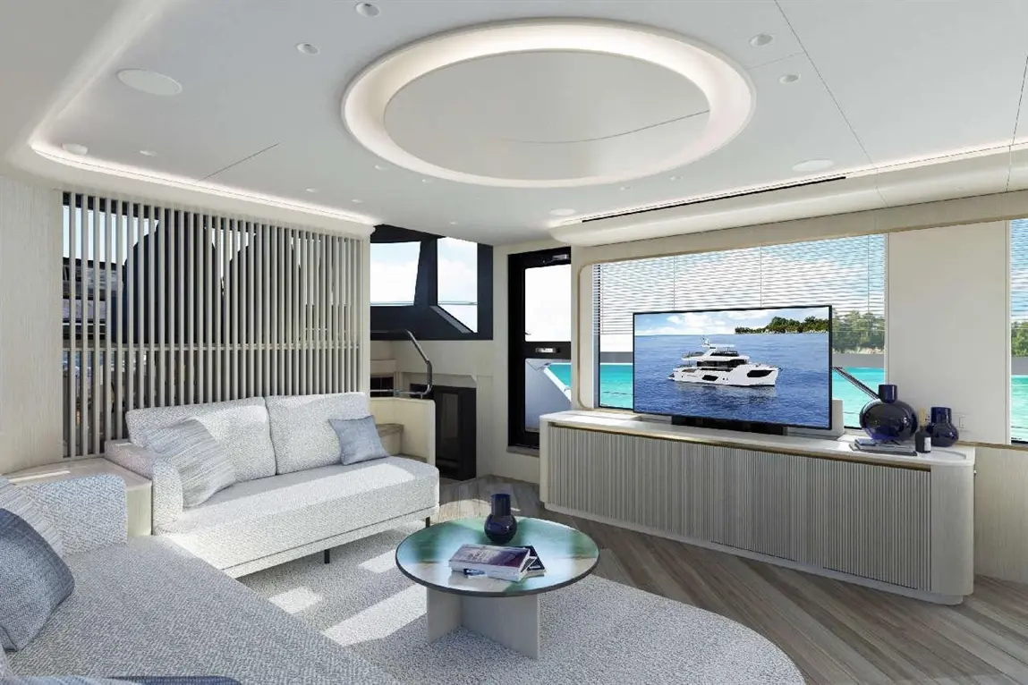 Stylish yacht living room featuring a grey sofa, glass coffee table, and large TV displaying a boat, with ocean views.