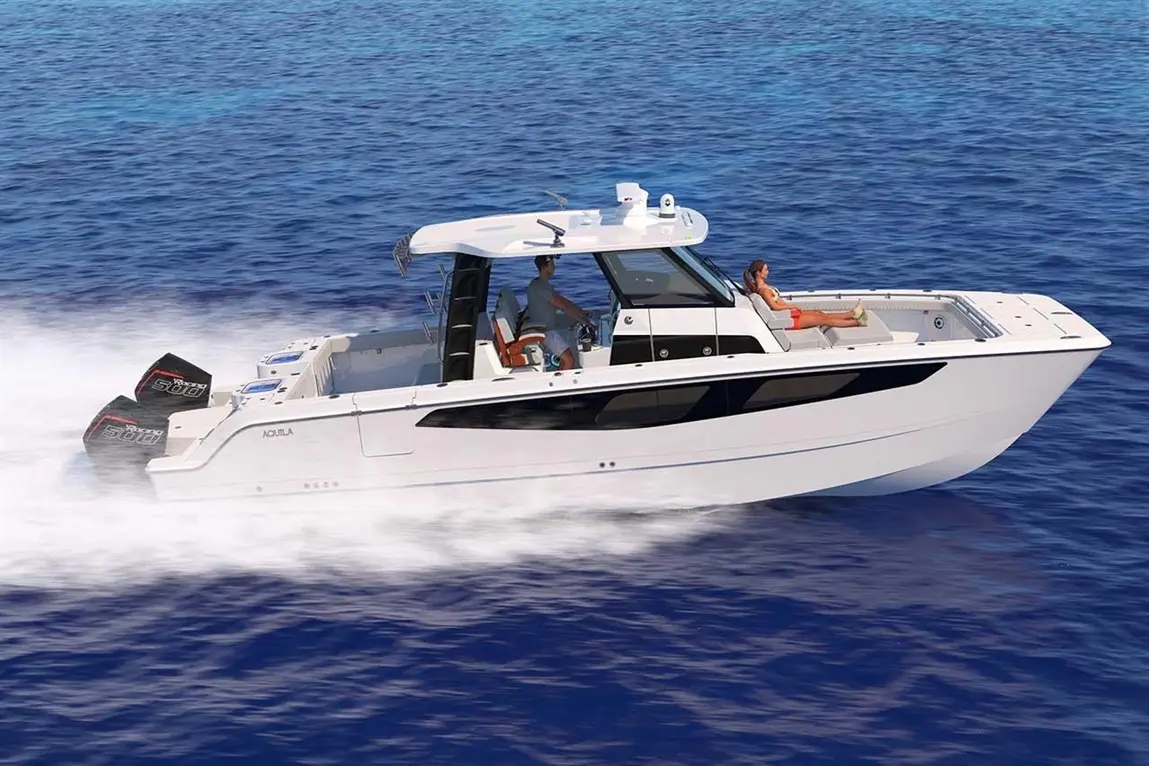 A cruising boat speeds across blue waters, with a man steering and a woman relaxing on board. Twin black motors visible.