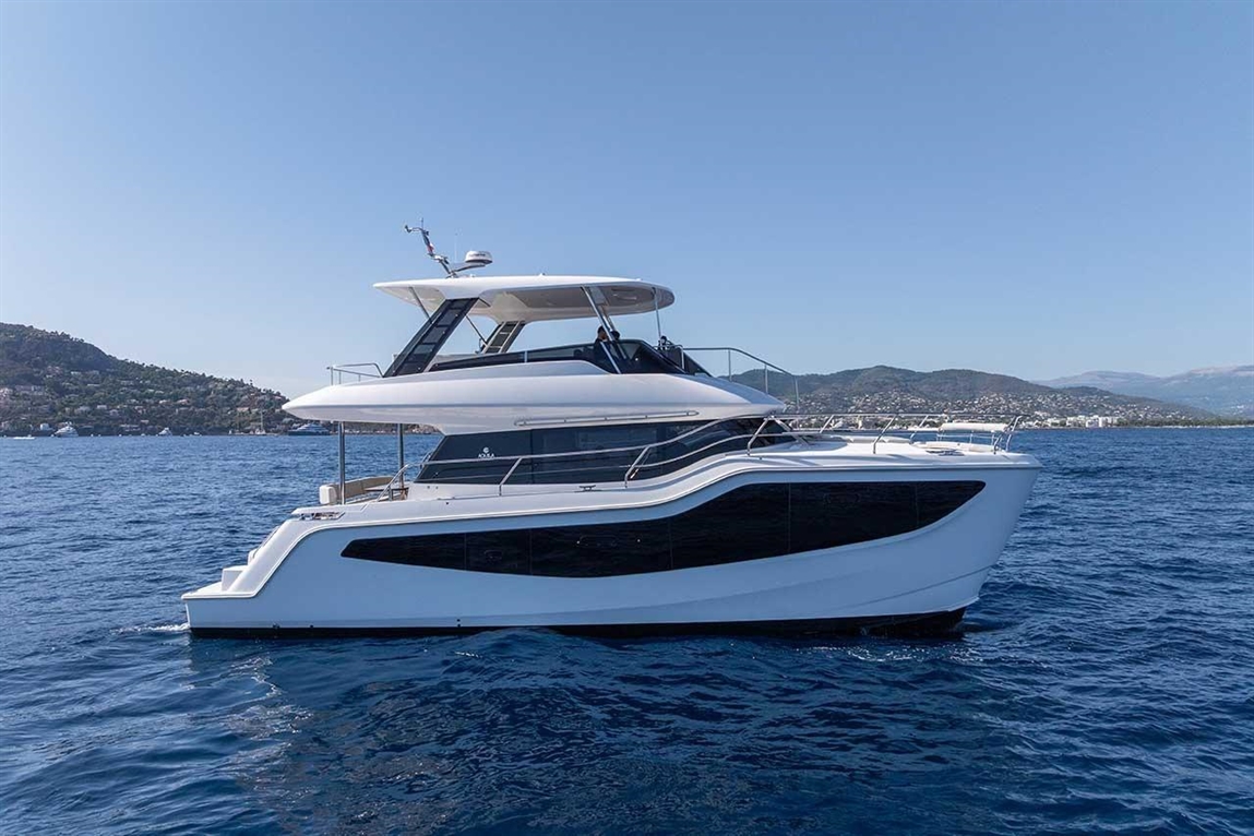 Luxurious white yacht gliding through blue waters with a hillside and coastline in the background on a clear day.