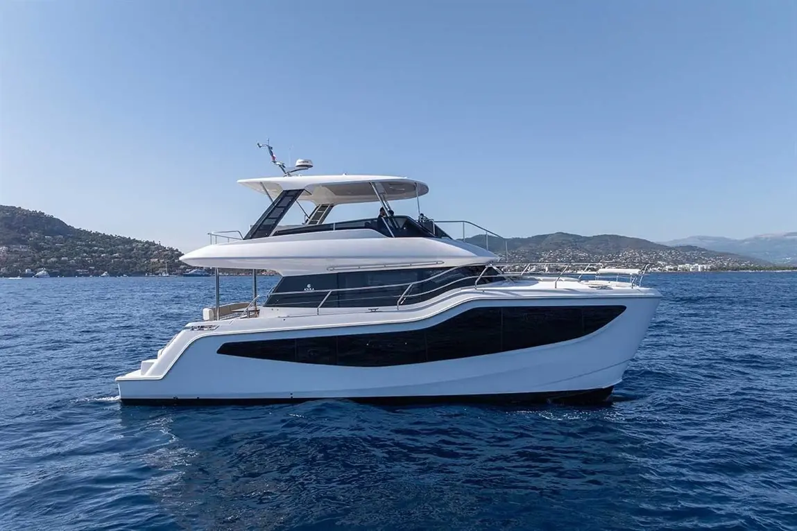 Luxurious white yacht gliding through blue waters with a hillside and coastline in the background on a clear day.