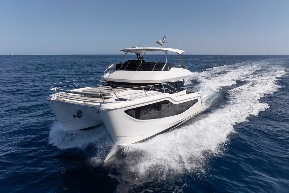Luxury catamaran cruising on calm blue waters, leaving a wake behind; modern design with sleek lines and large windows.