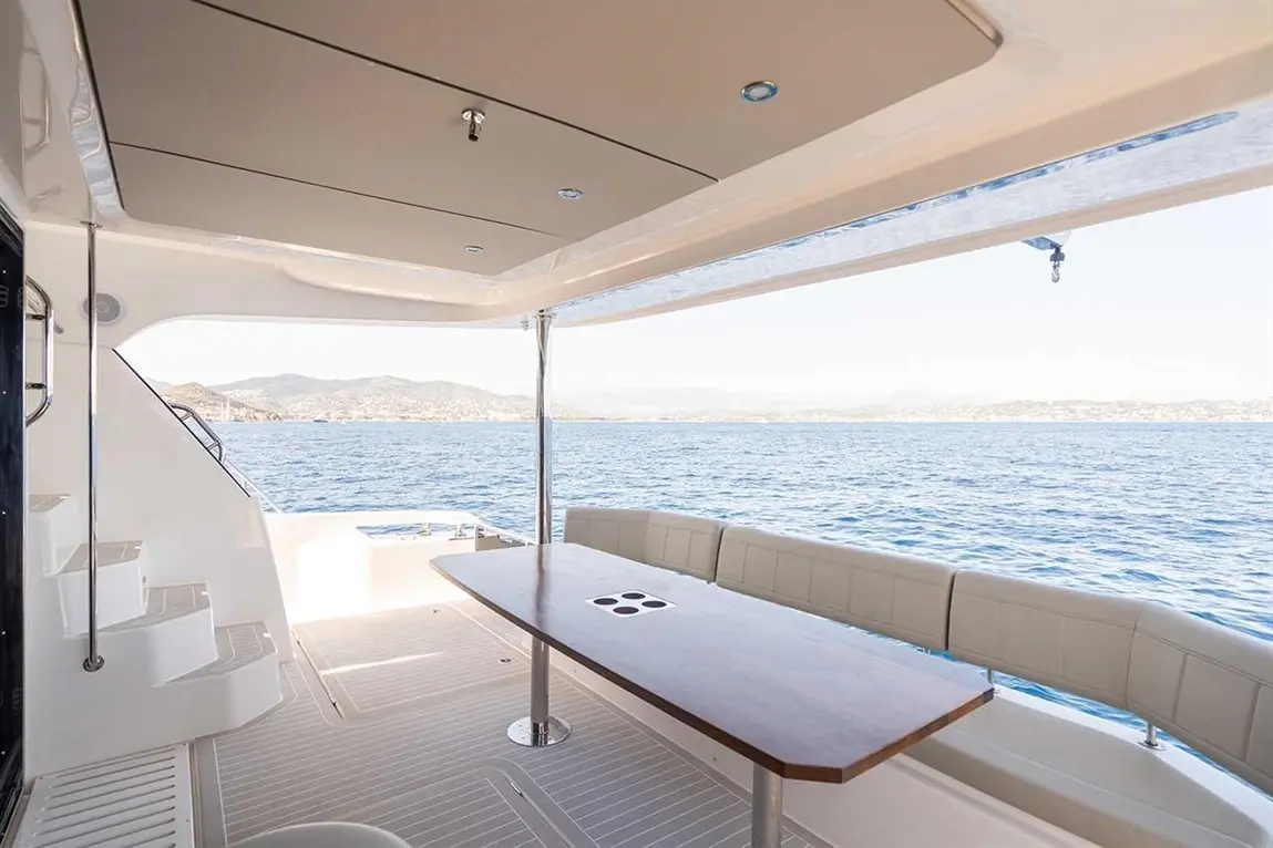 Interior of a luxury yacht with a wooden table, leather seating, and scenic ocean view through large windows.