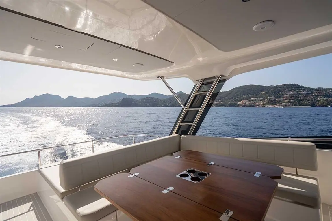 Luxury yacht interior with a wooden dining table, white seating, and scenic coastal mountains in the background.