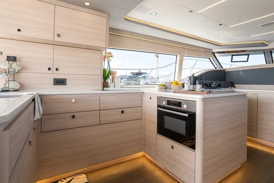 Modern yacht kitchen with light wood cabinetry, an oven, and a scenic window view of boats and the waterfront.