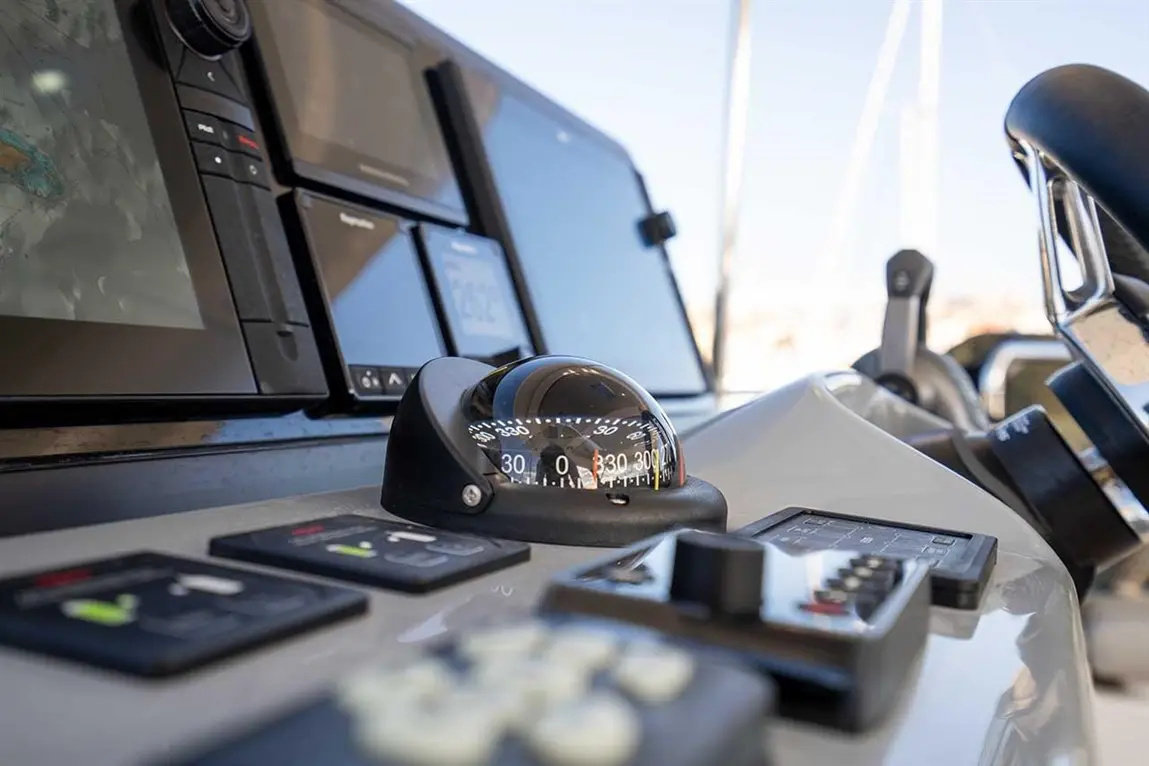 A close-up of a boat's control panel featuring a compass, navigation screens, and control buttons.