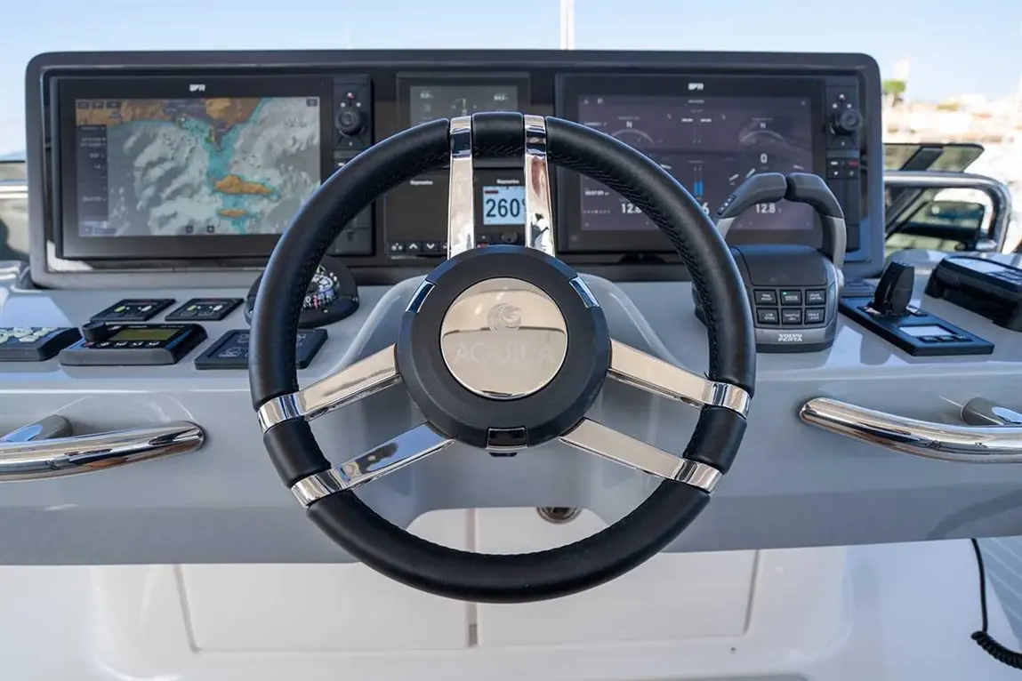 A close-up of a yacht's control panel featuring a steering wheel, navigation screens, and various buttons.