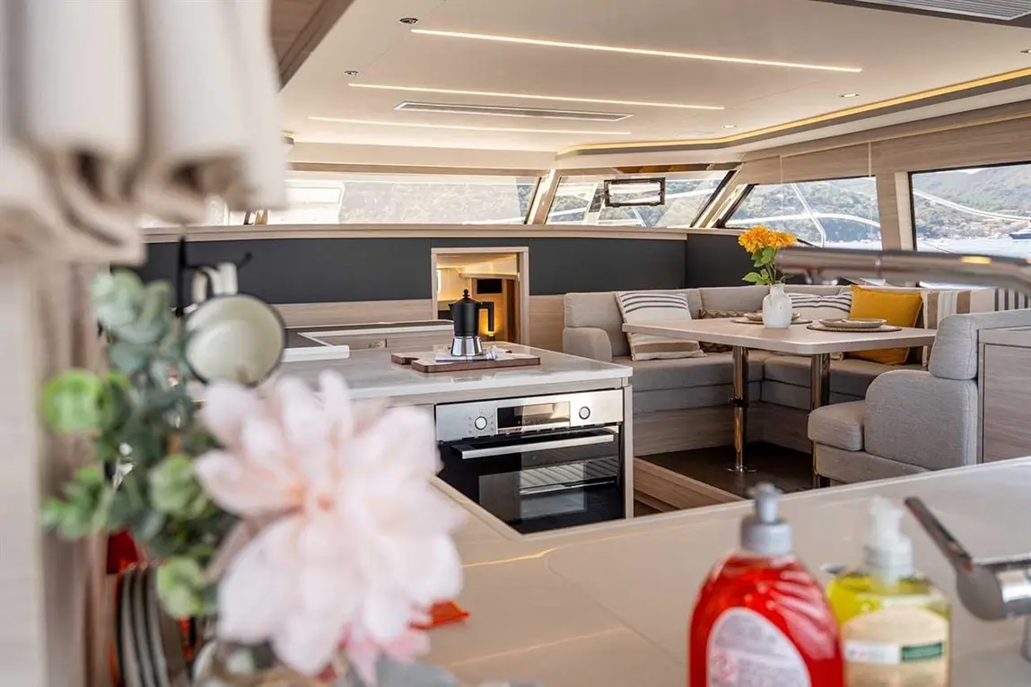 Modern yacht interior featuring a kitchen area, dining space, and a flower vase with striped cushions and views of the sea.