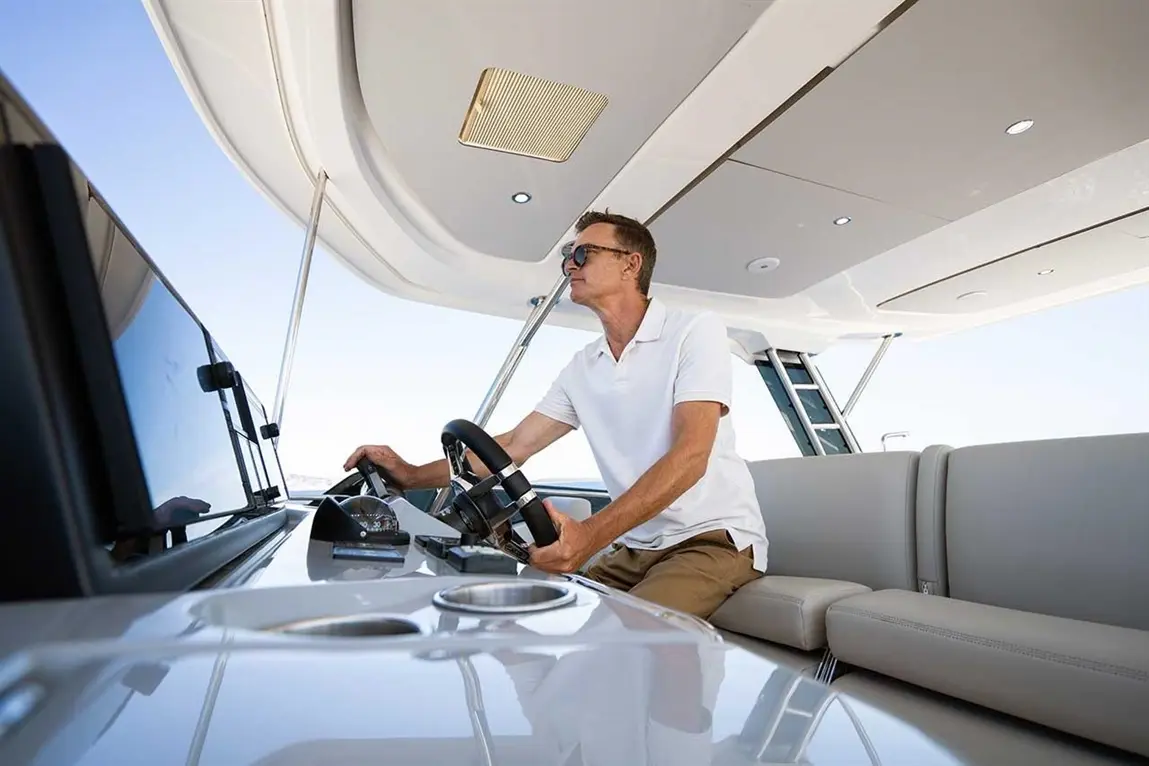 A man in a white polo shirt steers a motorboat from the helm, showcasing a modern dashboard and open sea view.