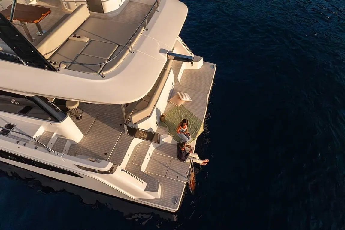 Aerial view of a luxury yacht with two people relaxing, one dangling feet off the edge, surrounded by deep blue water.