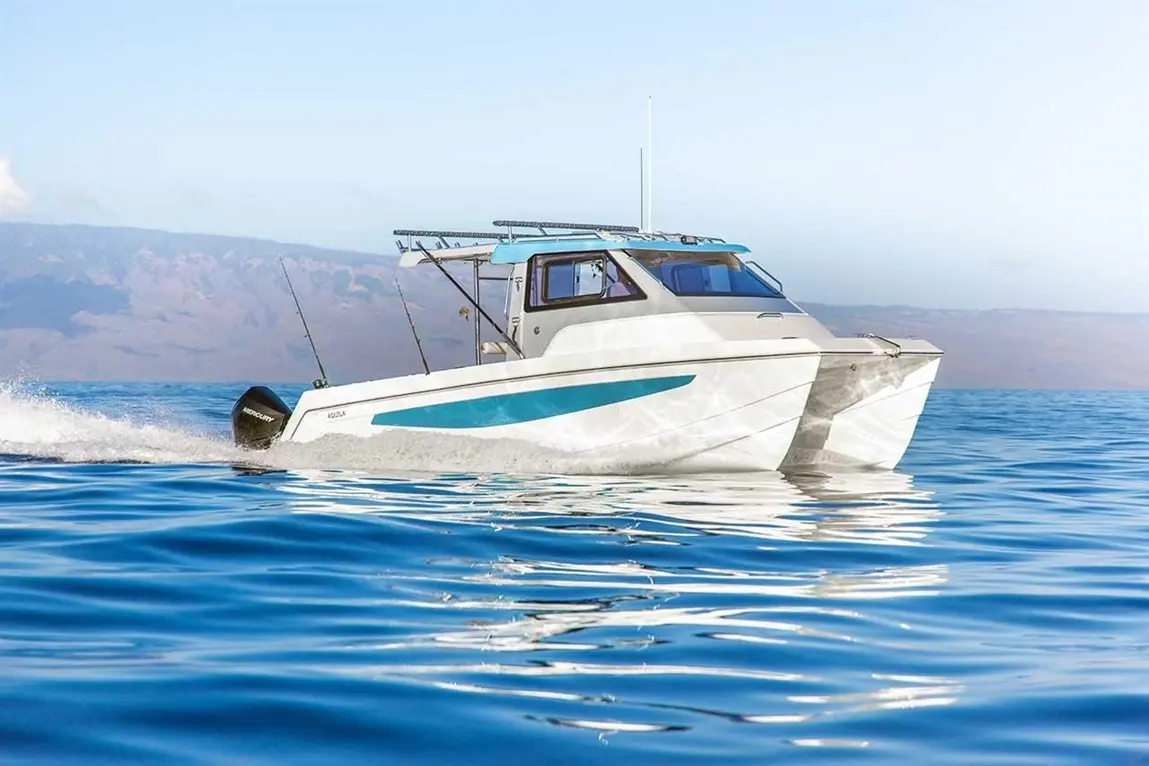 A sports fishing boat with a Mercury motor glides across calm blue waters, reflecting the sky and mountains in the background.