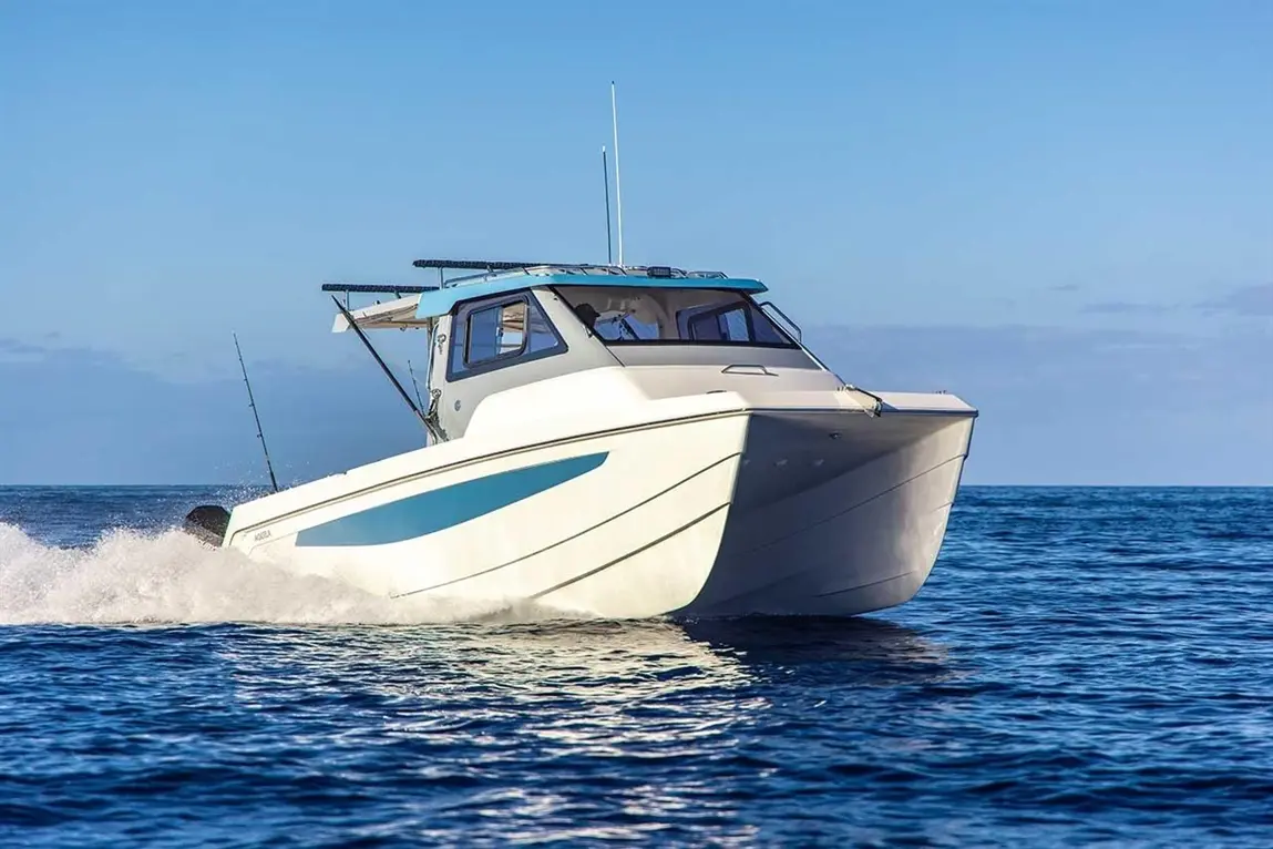 A white motorboat with a blue stripe speeds across the ocean, leaving a spray of water against a clear sky.
