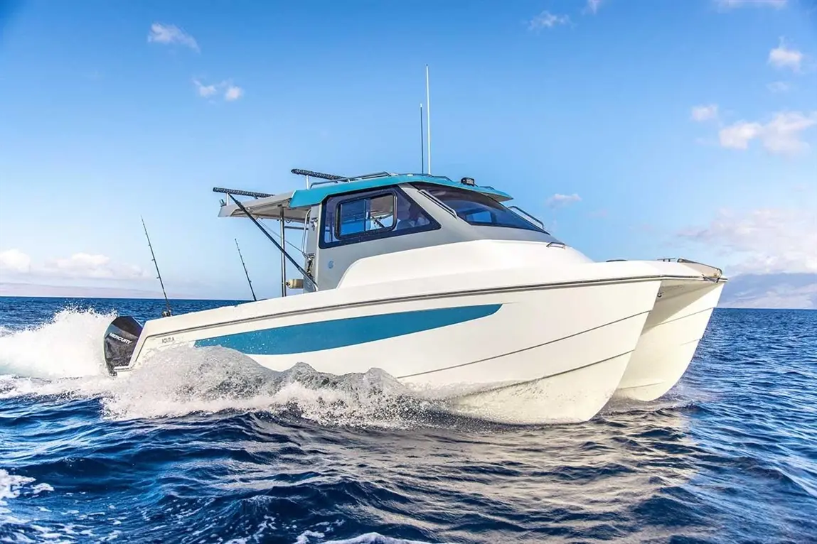 A sleek fishing boat with a blue accent speeding through ocean waters under a clear sky, featuring fishing rods attached.