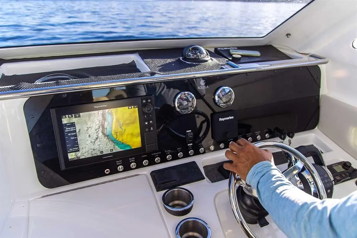 A close-up of a boat's control panel with a map display and a person steering, highlighting navigation and marine technology.