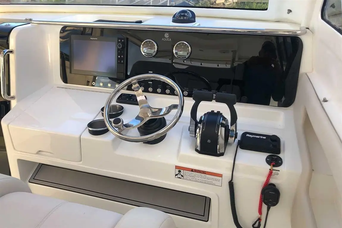 Boat dashboard featuring a steering wheel, monitors, controls, and cup holders; includes a warning label.