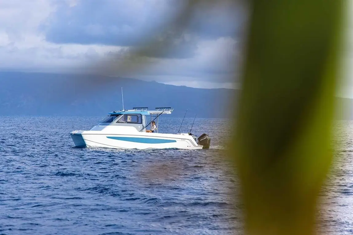 A white boat with blue accents is cruising on calm waters, surrounded by mountains and a partly cloudy sky.