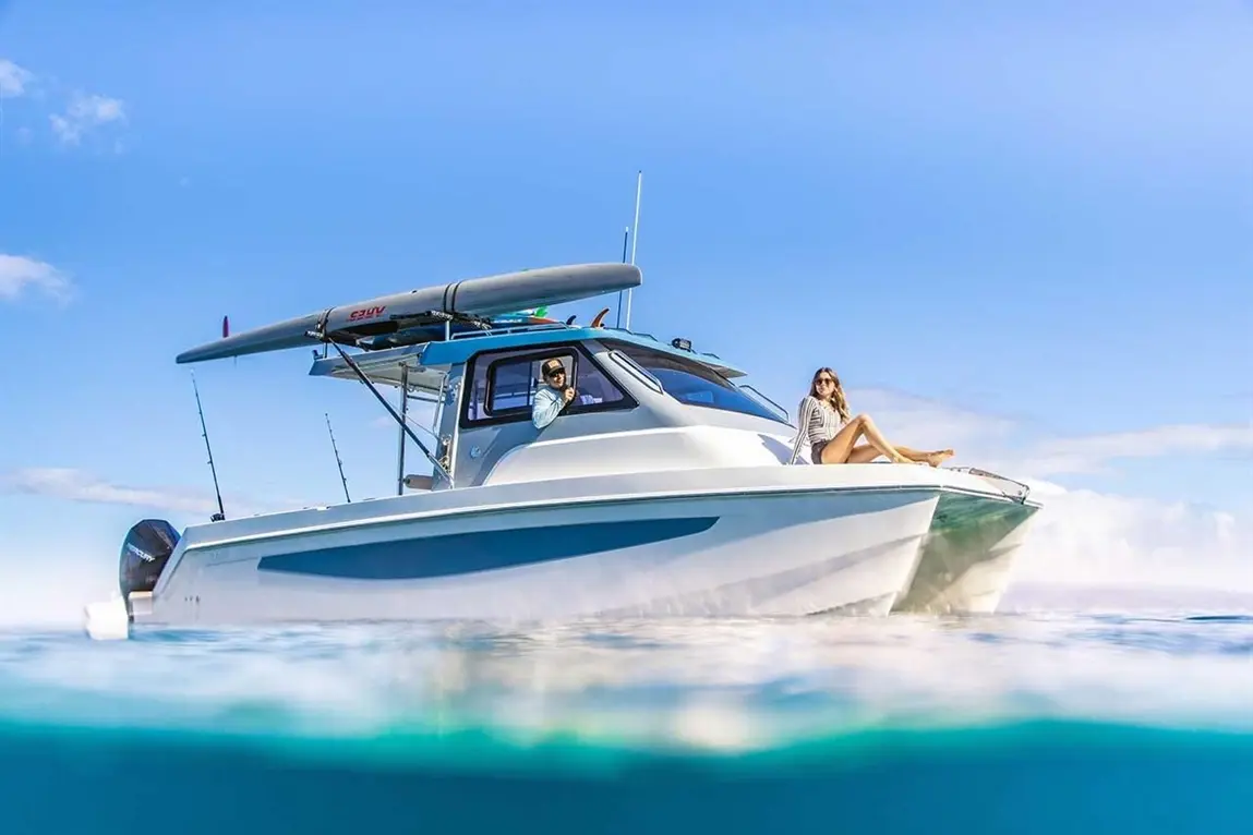 A sleek motorboat on clear water with two people aboard, one relaxing at the bow and the other steers.