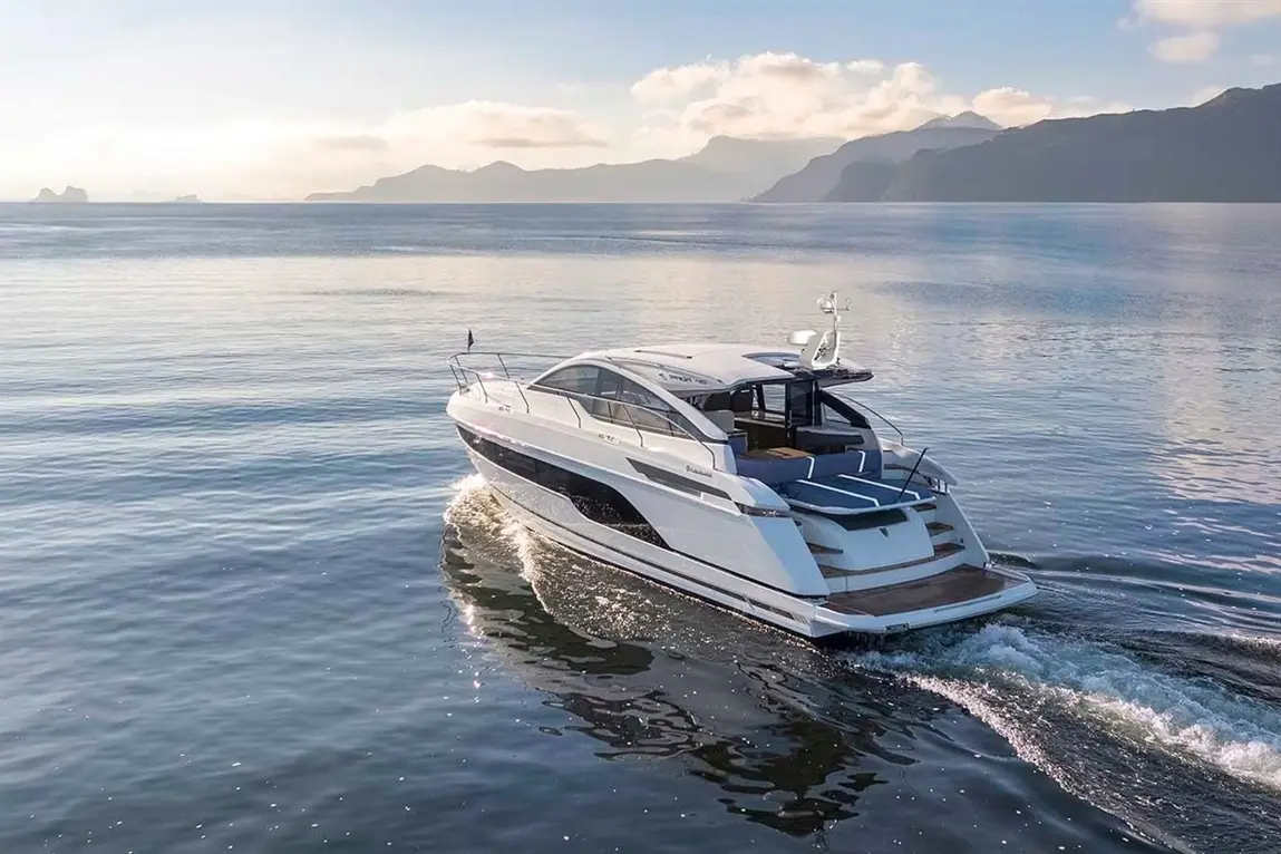 A sleek motor yacht glides across calm waters with mountains in the background, showcasing a tranquil maritime scene.