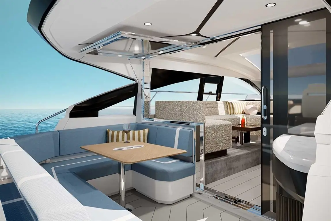 Luxury yacht interior featuring a seating area with blue cushions and a wooden table, overlooking the ocean through large windows.
