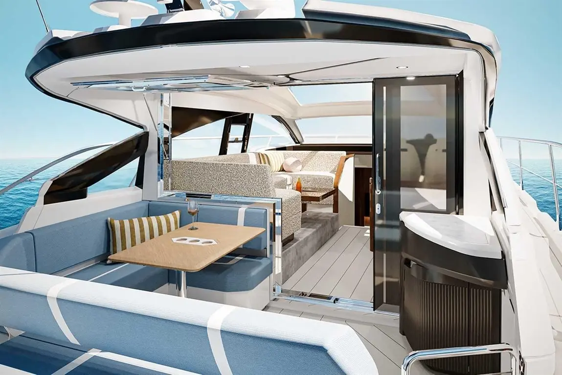 Modern yacht interior featuring a dining area, plush seating, and a door leading to an outdoor deck with sea views.