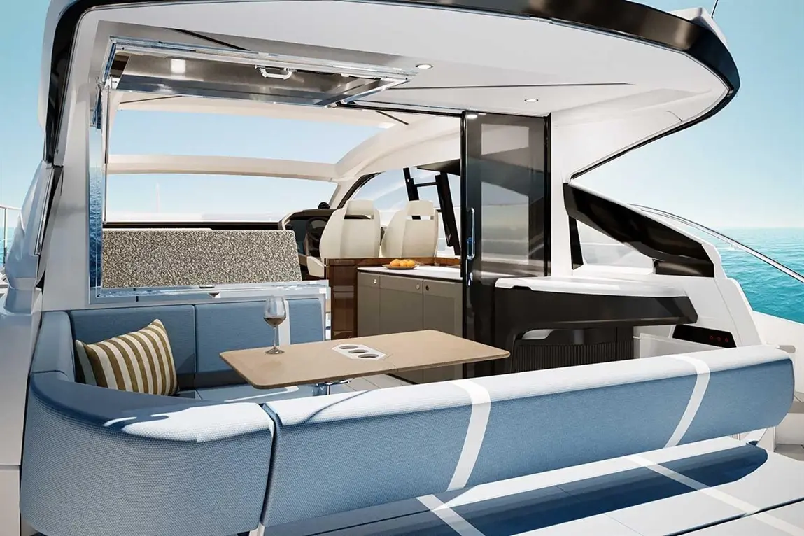 Modern yacht interior featuring a spacious lounge with blue upholstery, a dining table, and a view of the sea.