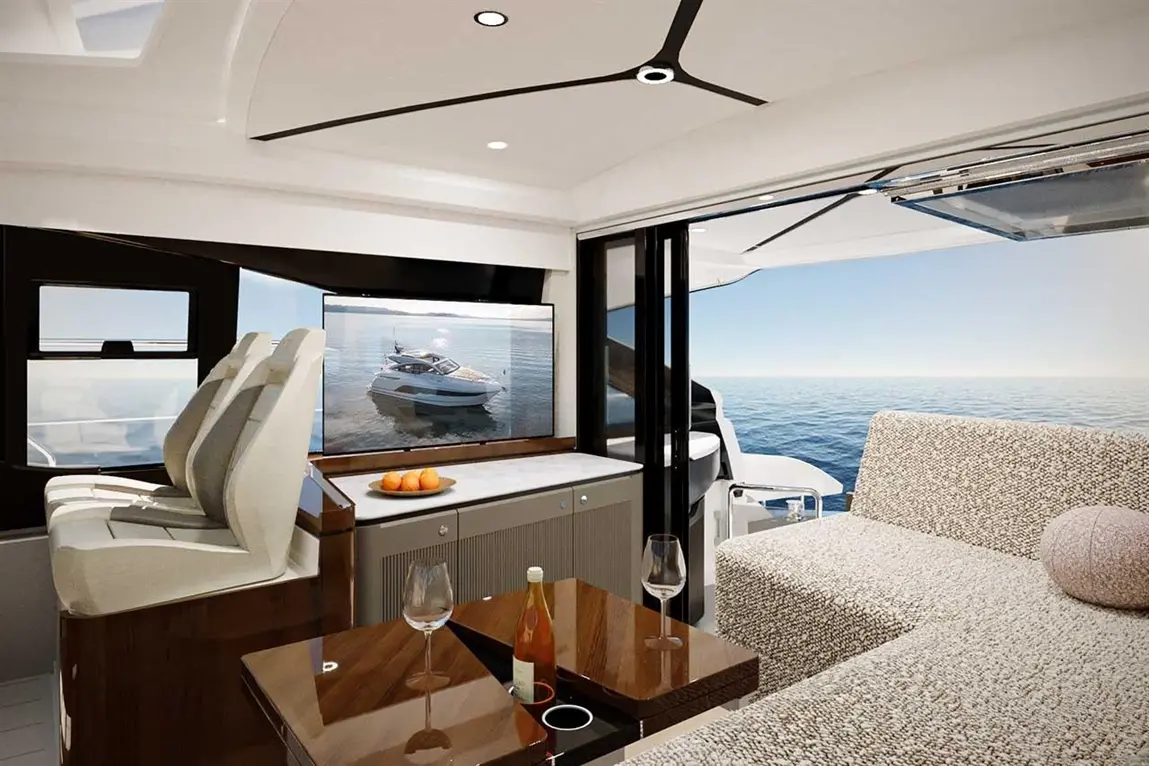 Luxurious yacht interior features plush seating, a large screen displaying a boat, and scenic ocean views from large windows.