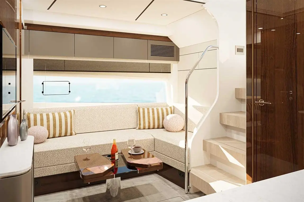 Modern yacht interior featuring a cosy seating area, glass table, and staircase, with scenic ocean views through the window.