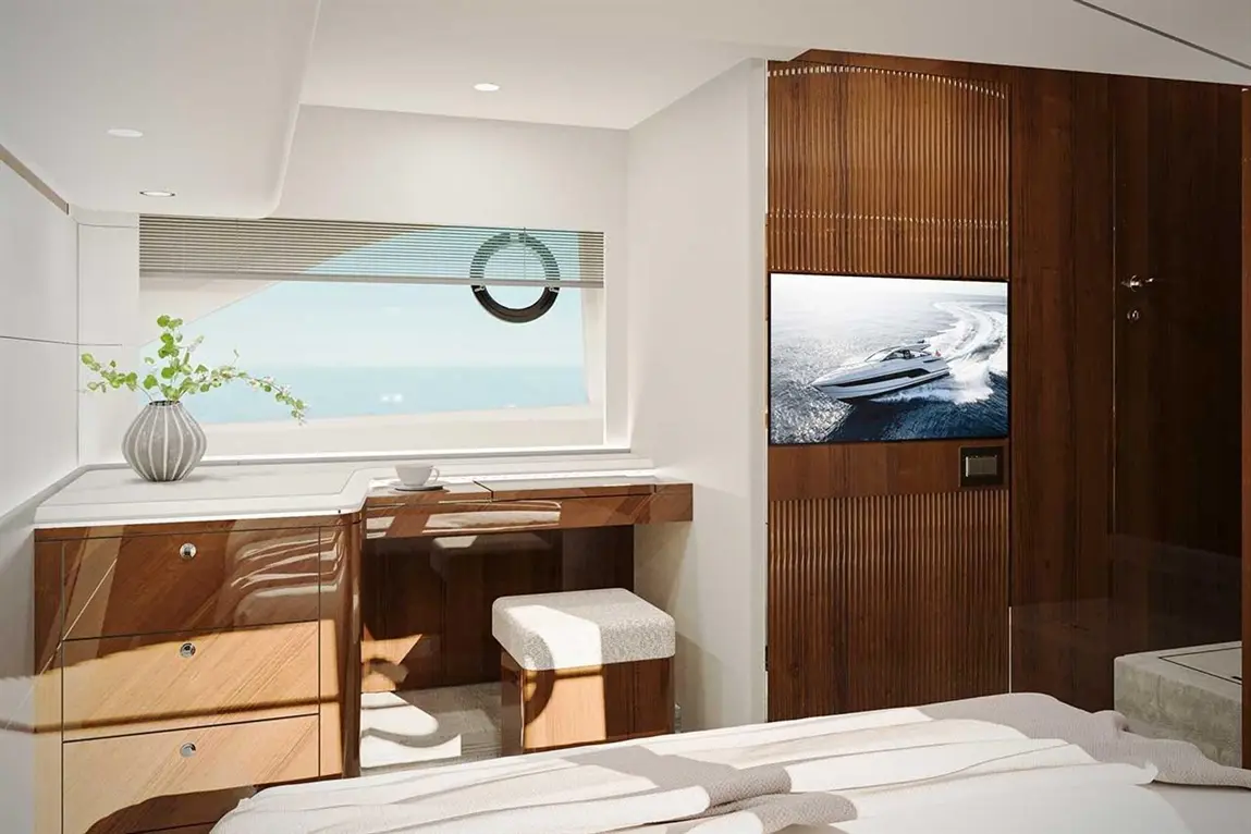 Modern yacht interior with a desk, TV showing a boat, decorative vase, and ocean view through a large window.