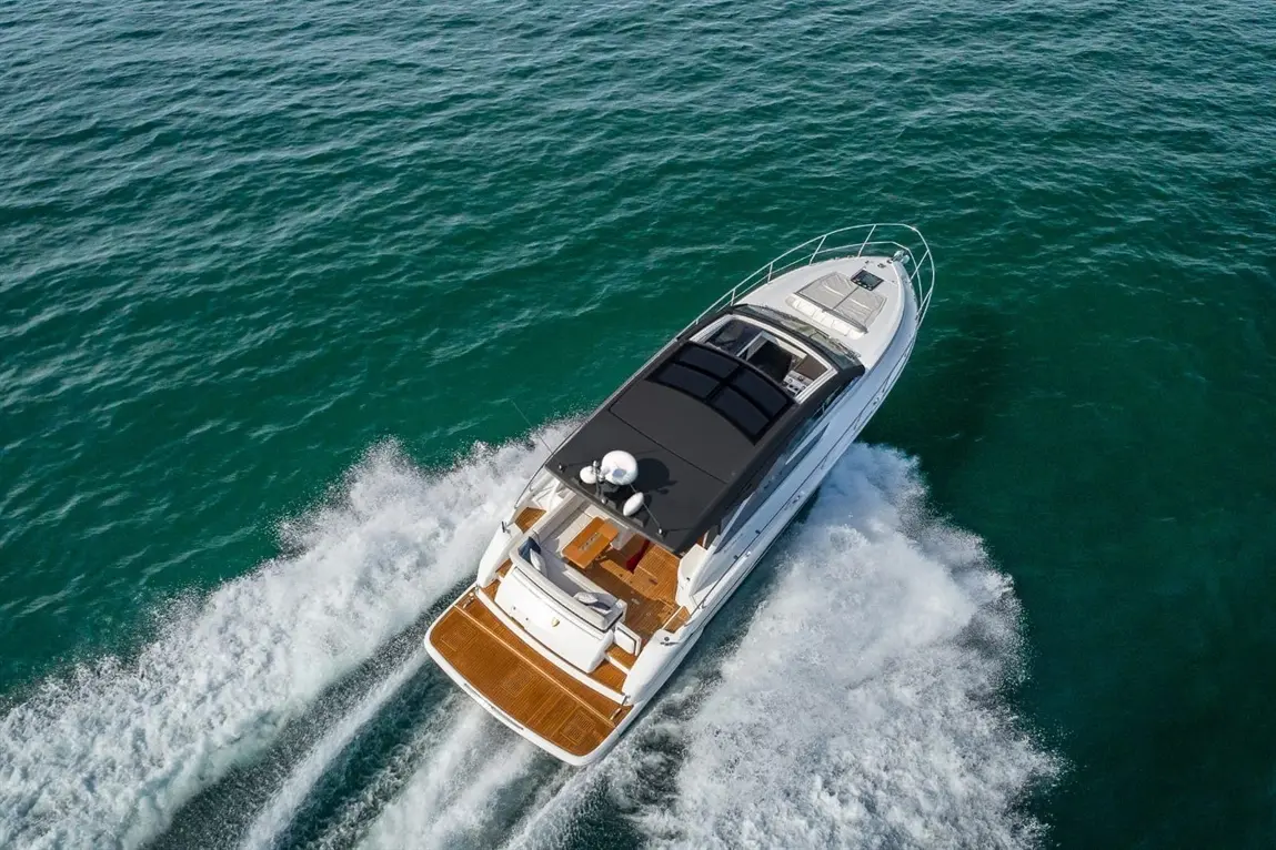 A sleek motorboat speeds through turquoise water, leaving a white wake behind; sunlight reflects off the vessel's surface.