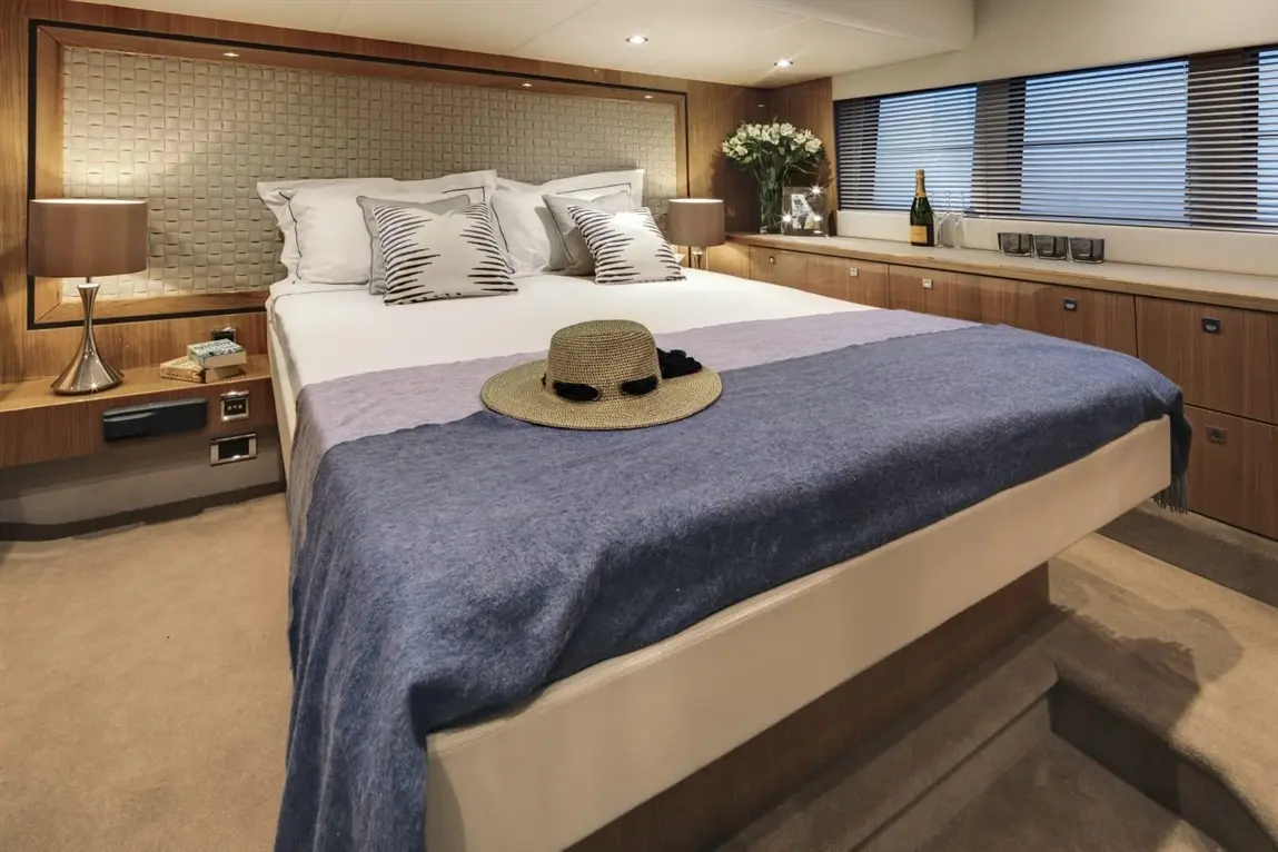 Stylish yacht bedroom featuring a double bed, decorative pillows, a straw hat, and a champagne bottle on a cabinet.