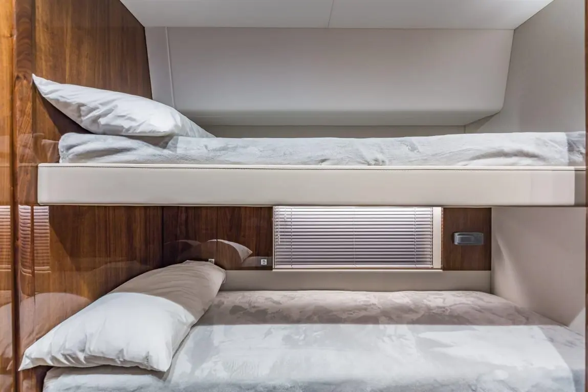 Bunk beds with soft bedding in a modern interior, featuring wooden panels and a window with blinds.