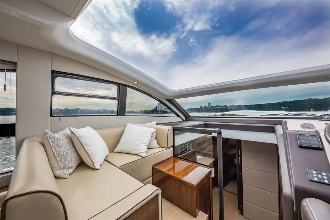 Luxury yacht interior featuring a beige sofa, white cushions, panoramic windows, and a wooden coffee table.