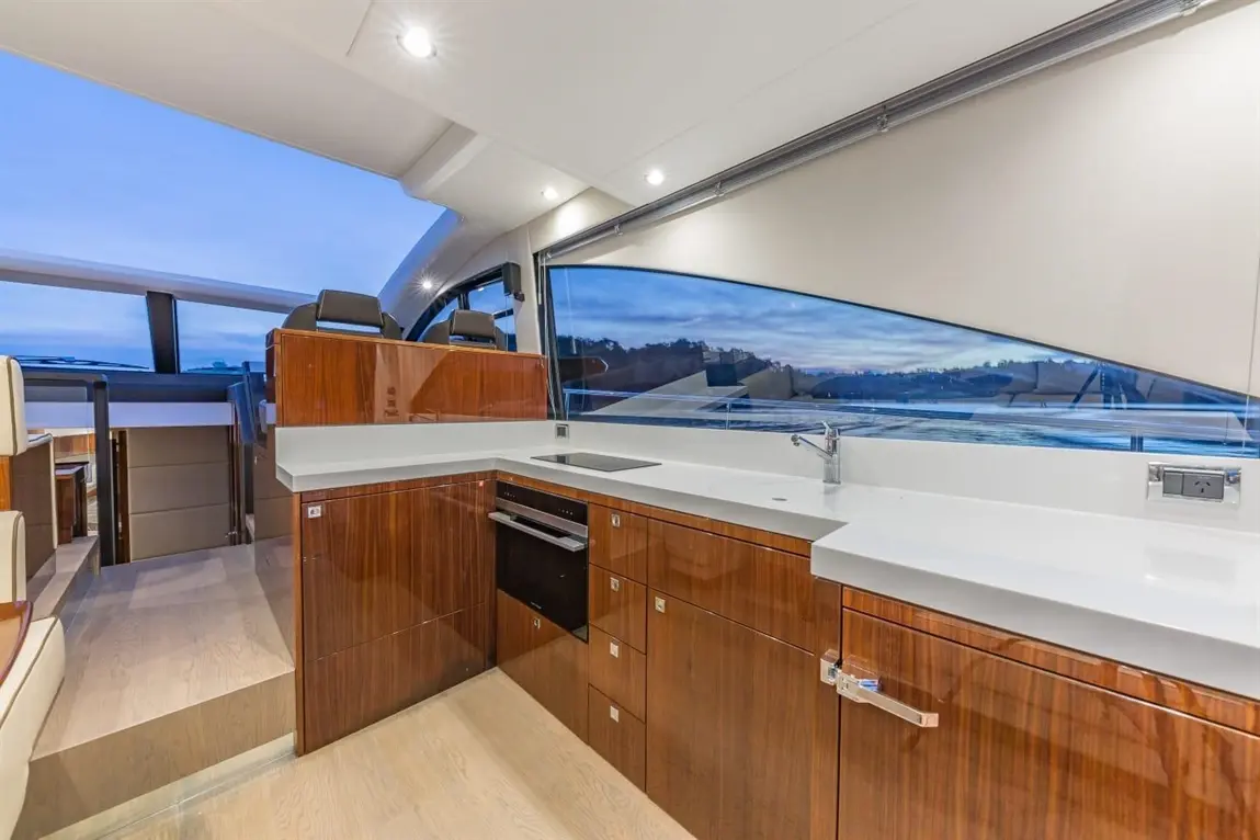 Modern yacht interior featuring a sleek kitchen with a white countertop, wooden cabinets, and large windows for natural light.