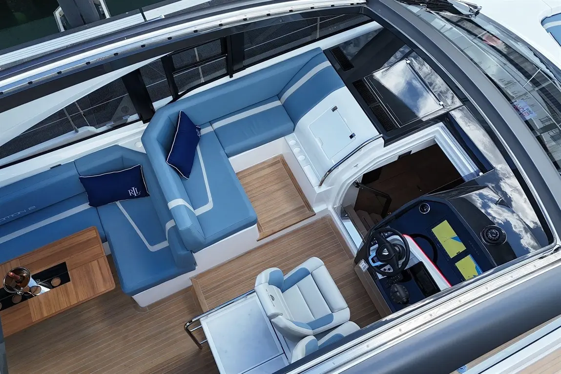 Luxury boat interior featuring blue seating, a helm with navigation displays, wooden flooring, and a dining table.