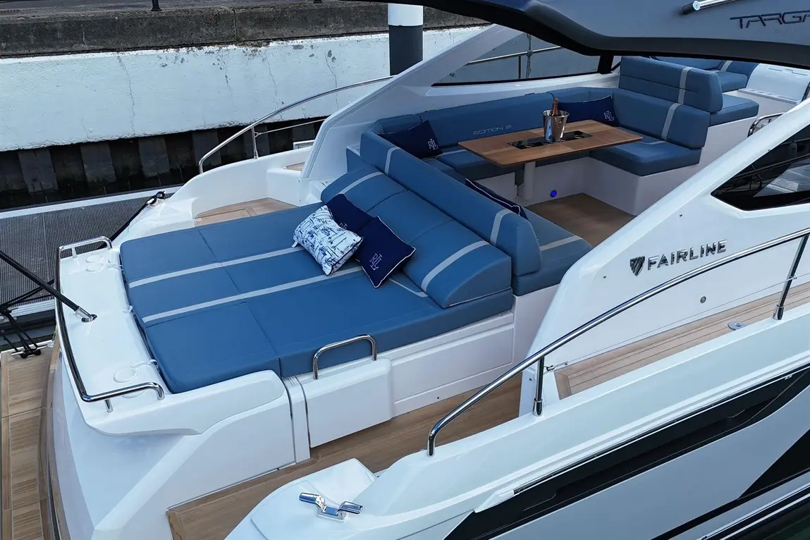 Stylish Fairline boat interior featuring blue cushions, a wooden table, and a champagne bucket on a modern deck by the water.