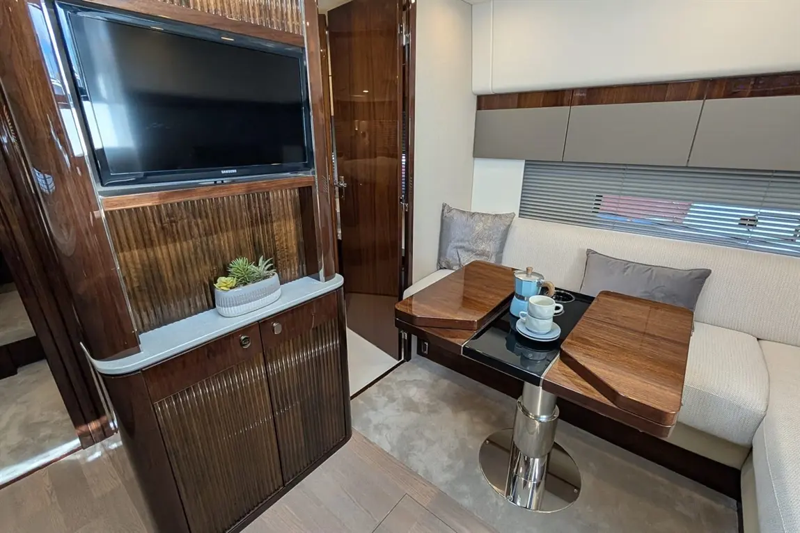 Luxurious interior of a yacht cabin with a curved table, coffee cups, TV, and modern decor. Elegant grey and wood accents.