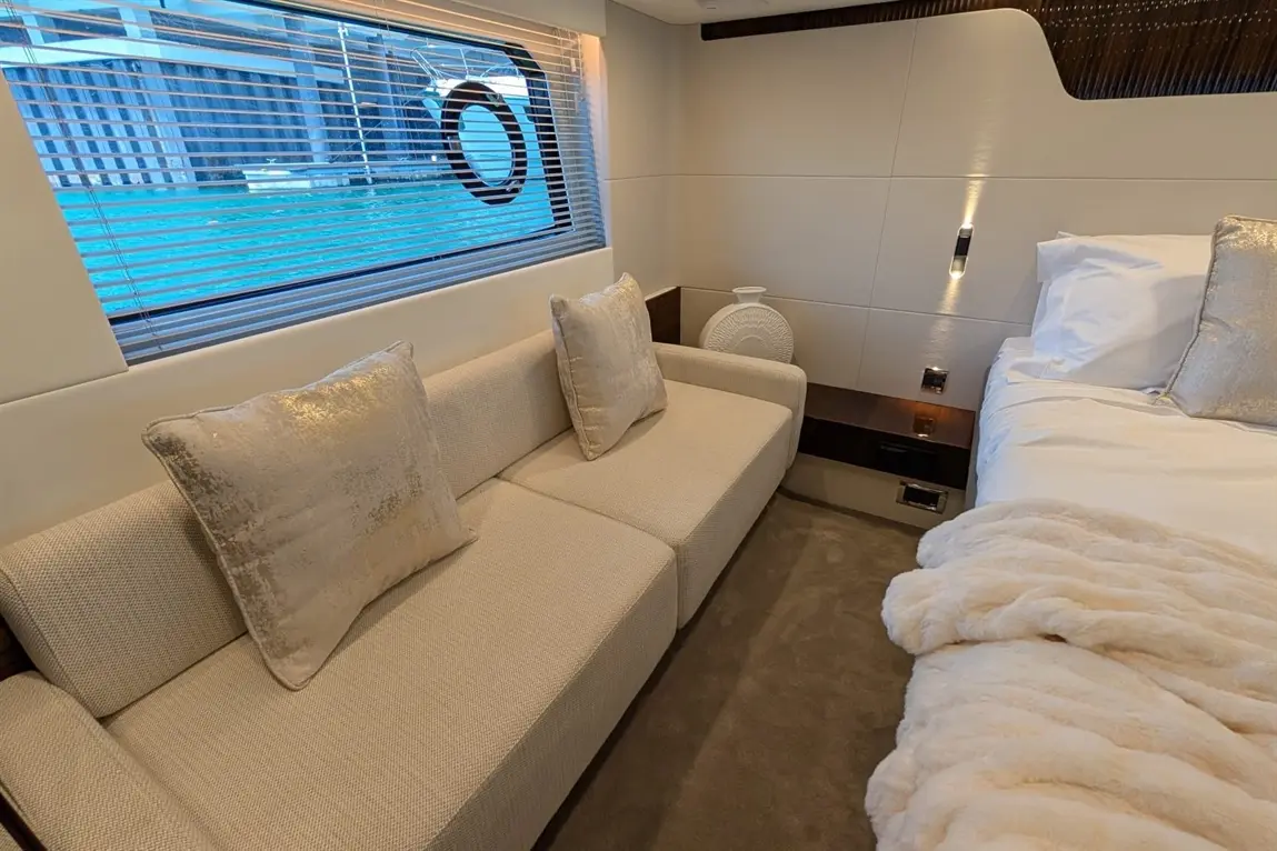 Modern bedroom with a plush sofa, decorative cushions, a bedside table, and natural light from the window overlooking water.