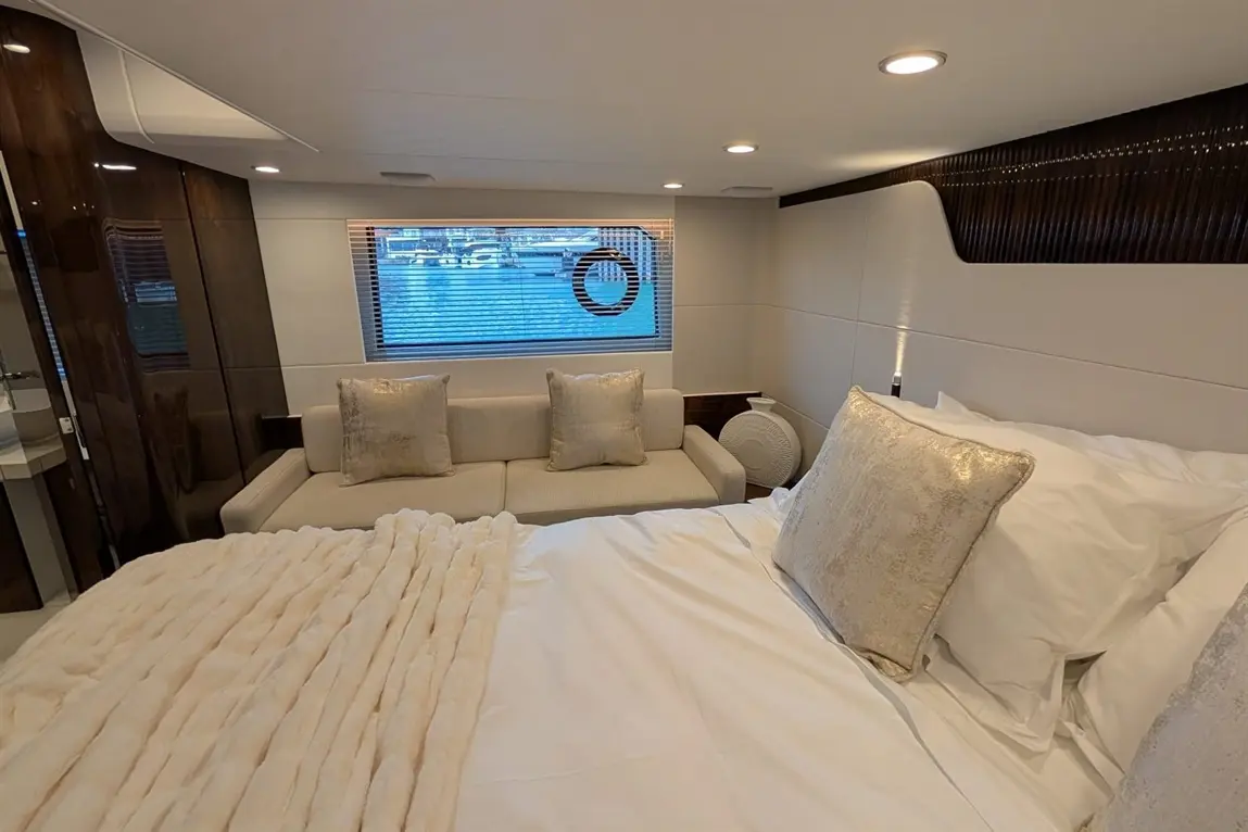 Luxury yacht interior featuring a plush bed, sofa with cushions, and a view through a window with blinds.