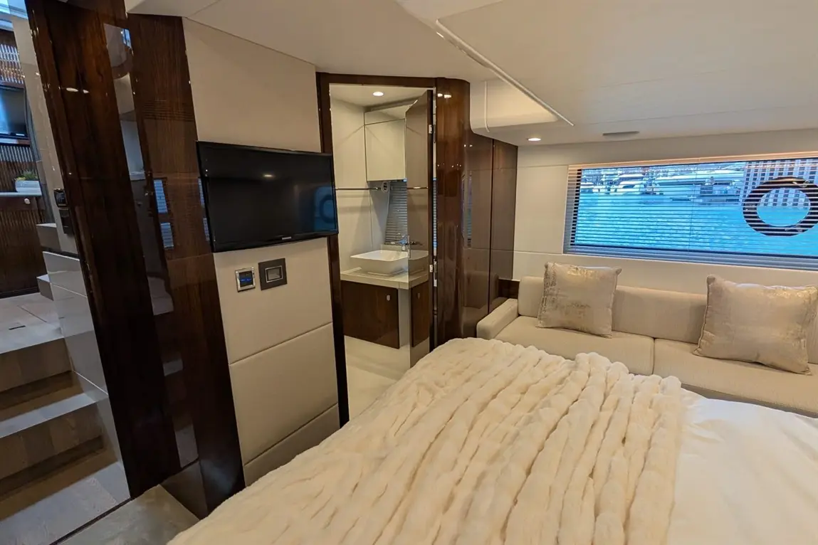 Luxurious yacht interior featuring a plush bed, modern TV, and stylish seating area with a view of the water through large windows.