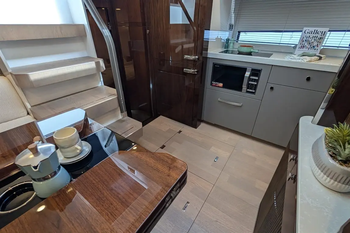 Modern yacht interior featuring stairs, kitchenette with microwave, coffee pot on a table, and decorative plants.
