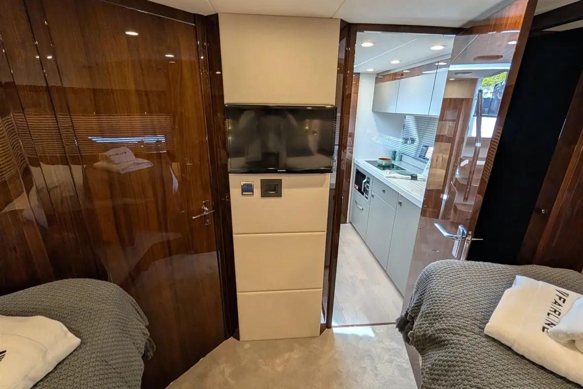 Luxury yacht interior featuring a kitchen, TV, twin beds, and stylish wooden finishes. Towel with "FAIRLINE" visible.