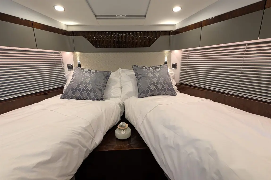 Modern twin bedroom with white bedding, decorative grey pillows, and bedside lamps, featuring a stylish decorative item on a table.