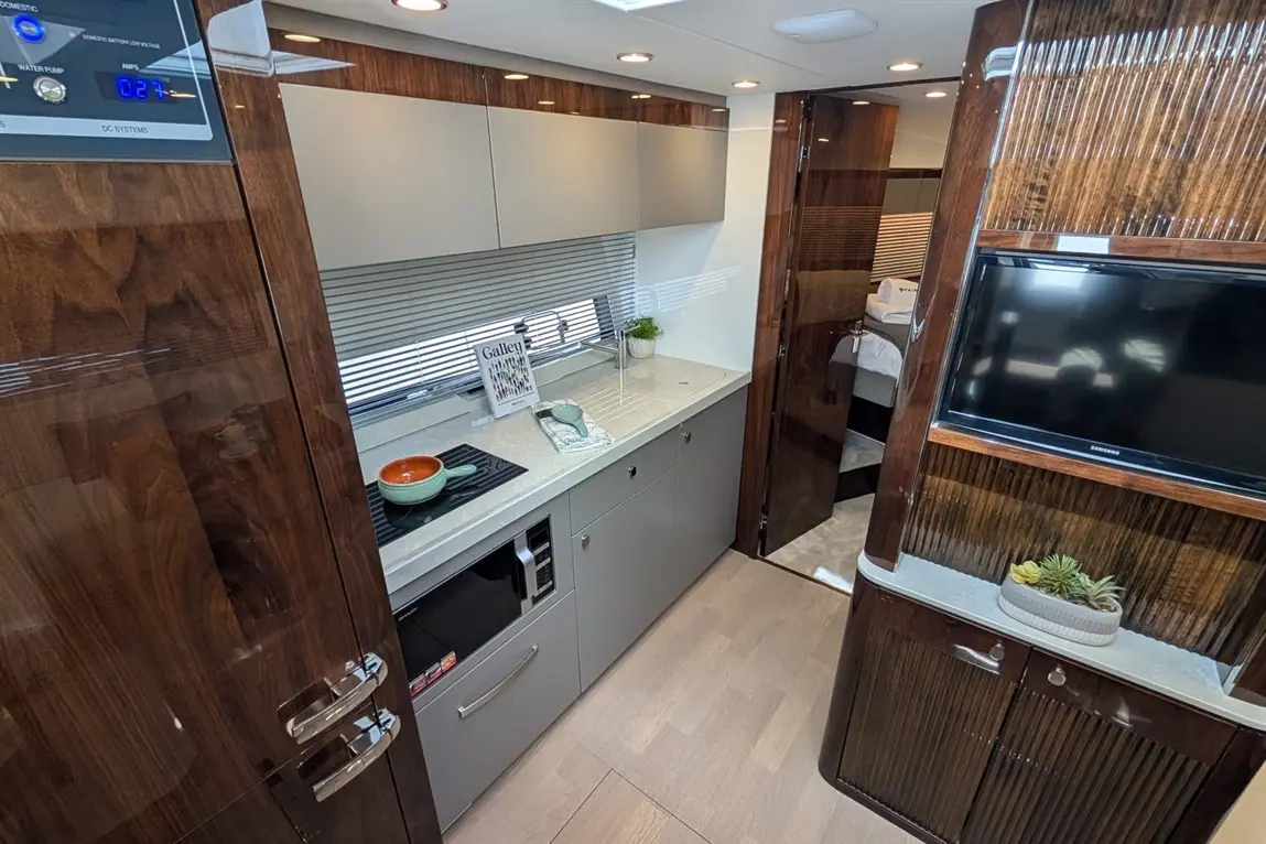 Modern boat galley with sleek cabinets, cooking area, microwave, and stylish decor, featuring a plant and a recipe book titled "Galley.