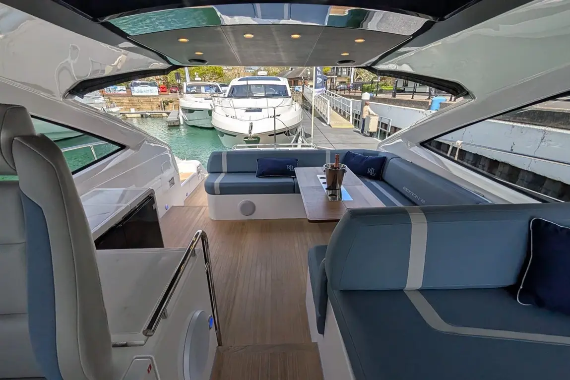 Interior of a luxury boat with seating, a table, an ice bucket, and views of nearby yachts and a marina.
