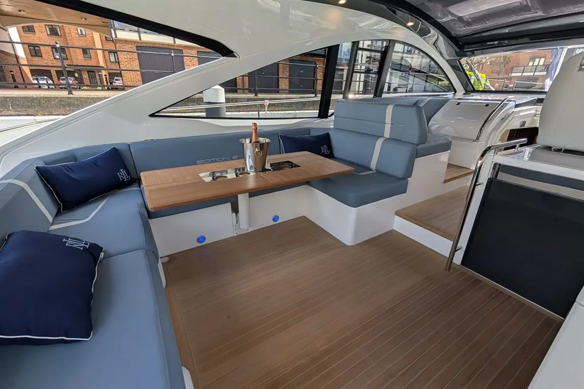 Luxurious yacht interior featuring a seating area, wooden table, and champagne cooler, with stylish blue cushions and steps.